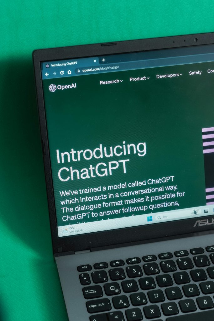 A close-up shot of an ASUS laptop with a black keyboard, displaying the OpenAI website’s 'Introducing ChatGPT' page on a green screen. The text describes how ChatGPT, an AI-powered language model, interacts in a conversational format. This image highlights a milestone in the evolution of artificial intelligence in history, showcasing the impact of AI-driven tools in shaping modern communication and technology.