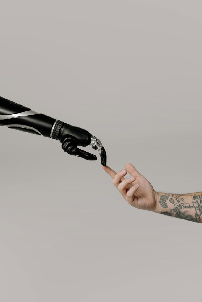 A futuristic scene of a sleek black robotic hand reaching out to touch a tattooed human hand, symbolizing the connection between artificial intelligence and humanity. As automation and AI integration grow, opportunities in Remote AI Jobs: How to Build a Career in Artificial Intelligence from Anywhere are expanding, allowing professionals to work in AI development, machine learning, and robotics from anywhere in the world.